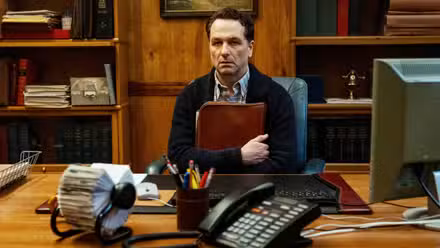 Matthew Rhys gripping a bag and staring dully ahead in Widow's Bay