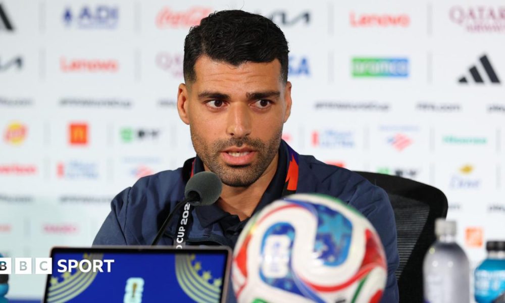Mehdi Taremi speaks into a microphone while conducting a press conference