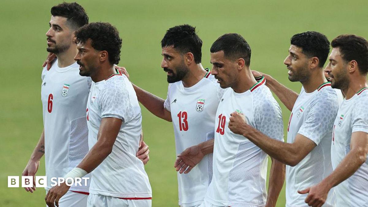 Six Iran players, wearing white Iran shirts, stand in a line