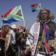 Hundreds of protesters marching outdoors, chanting and holding south african flags and signs