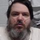 A man with black hair and a long black/grey beard has a breathing tube in his nose