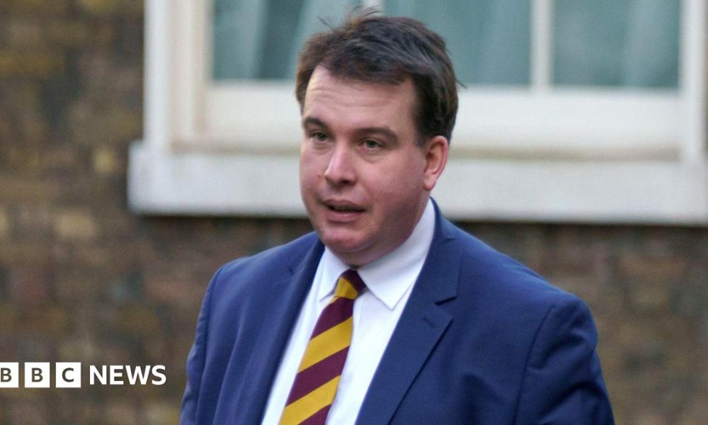 A head and shoulders shot of Craig Williams walking in the street wearing a navy suit and red and yellow striped tie. He has short brown hair. Image taken in February 2023.