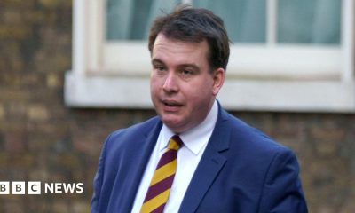 A head and shoulders shot of Craig Williams walking in the street wearing a navy suit and red and yellow striped tie. He has short brown hair. Image taken in February 2023.