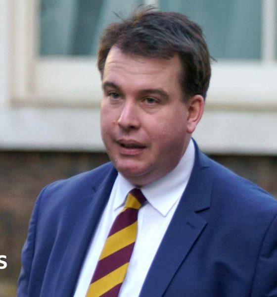A head and shoulders shot of Craig Williams walking in the street wearing a navy suit and red and yellow striped tie. He has short brown hair. Image taken in February 2023.