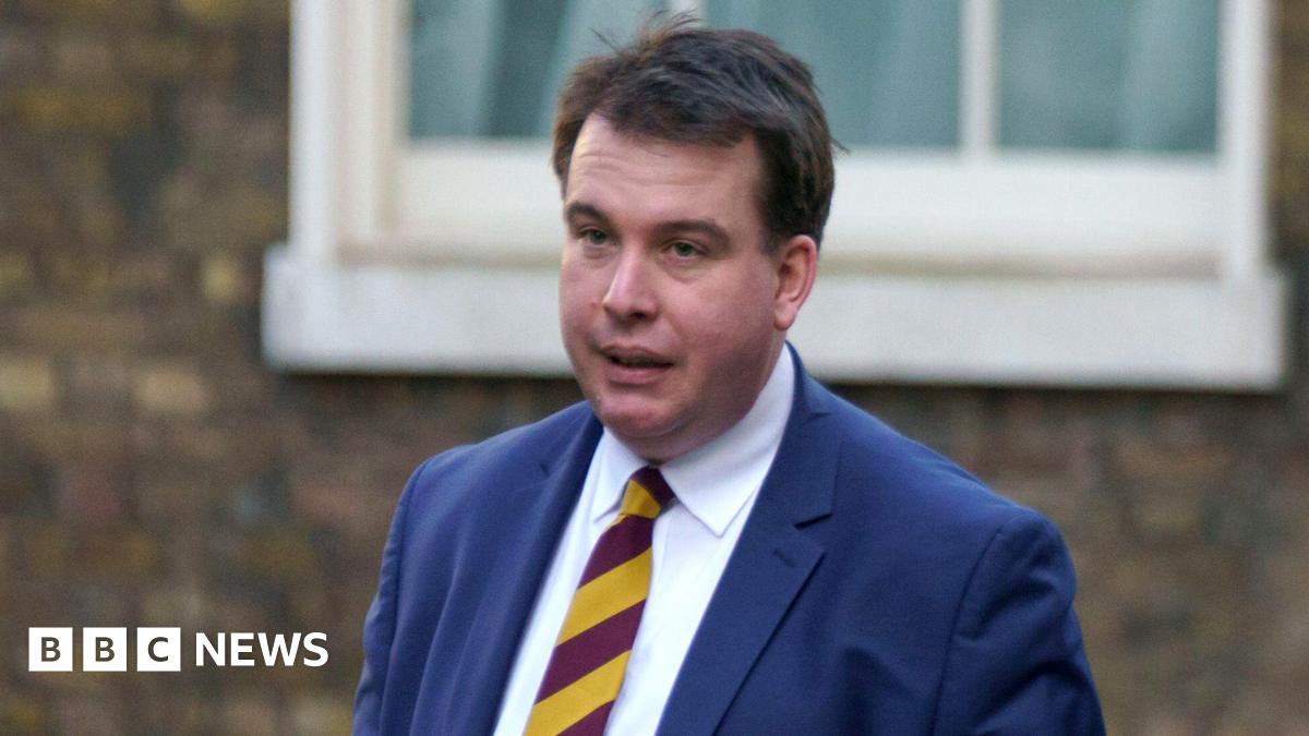 A head and shoulders shot of Craig Williams walking in the street wearing a navy suit and red and yellow striped tie. He has short brown hair. Image taken in February 2023.