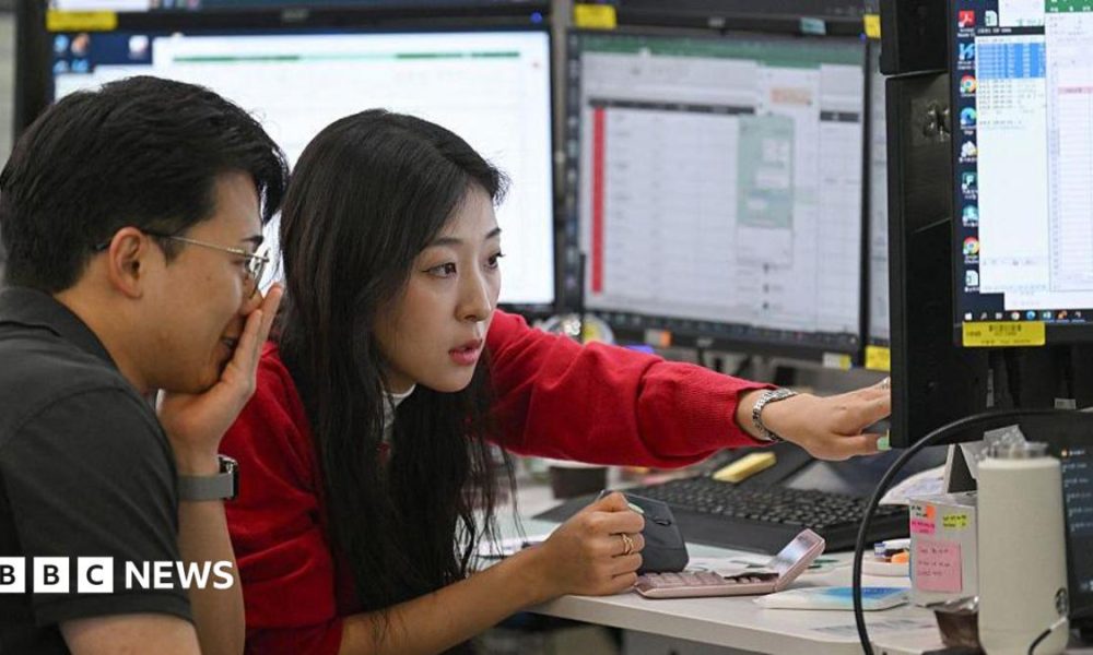 A woman in a red cardigan points to a screen during a discussion with a colleague in a trading room in Seoul