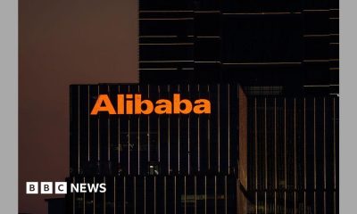 The Alibaba logo in orange lights is displayed on the exterior of an office that appears with black windows at dusk.