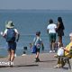 family walking along a coastal prominade.  one woman sitting on a bench looking out to sea.