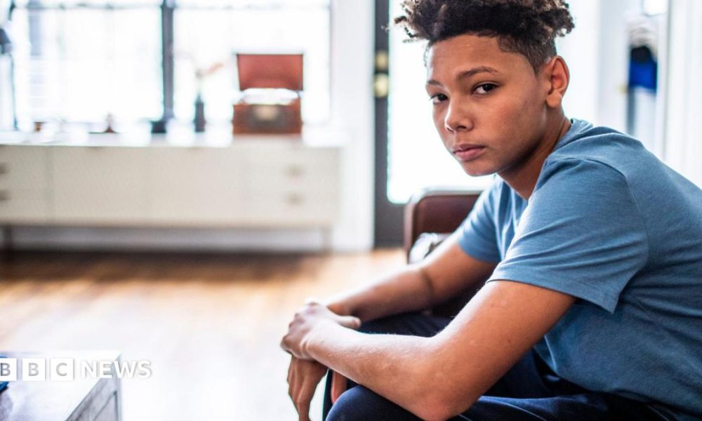 An anxious-looking teenager sits in a room, looking at the camera.
