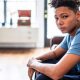An anxious-looking teenager sits in a room, looking at the camera.