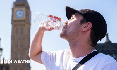 A man drinks from a water bottle with a sunny sky overhead and a blurred view of the Westminster skyline in the background