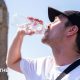 A man drinks from a water bottle with a sunny sky overhead and a blurred view of the Westminster skyline in the background