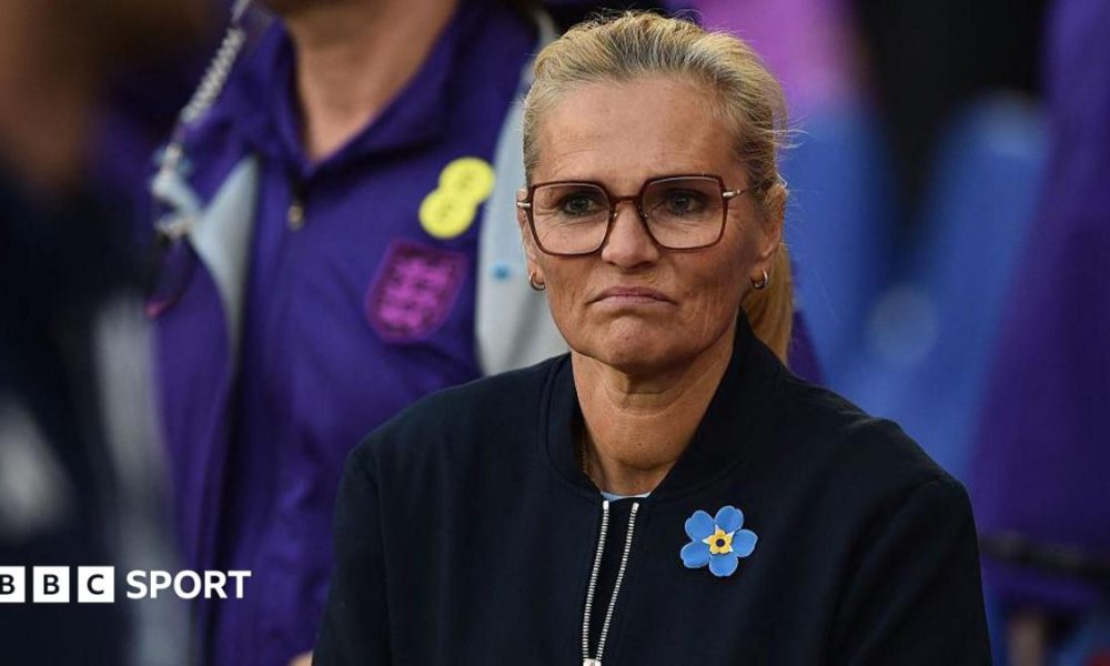 A frowning Sarina Wiegman in dark top and yellow and blue broach