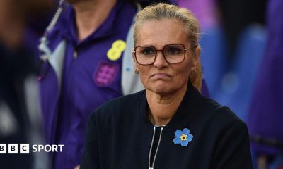 A frowning Sarina Wiegman in dark top and yellow and blue broach