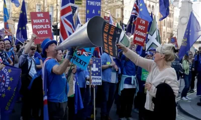 A supporter of Britain's departure from the European Union, at right, holds a placard up in front of supporters of remaining in the EU, including Stop Brexit Man, Steve Bray, with his foghorn, outside Parliament in London, Wednesday, Feb. 27, 2019.
