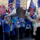 A supporter of Britain's departure from the European Union, at right, holds a placard up in front of supporters of remaining in the EU, including Stop Brexit Man, Steve Bray, with his foghorn, outside Parliament in London, Wednesday, Feb. 27, 2019.