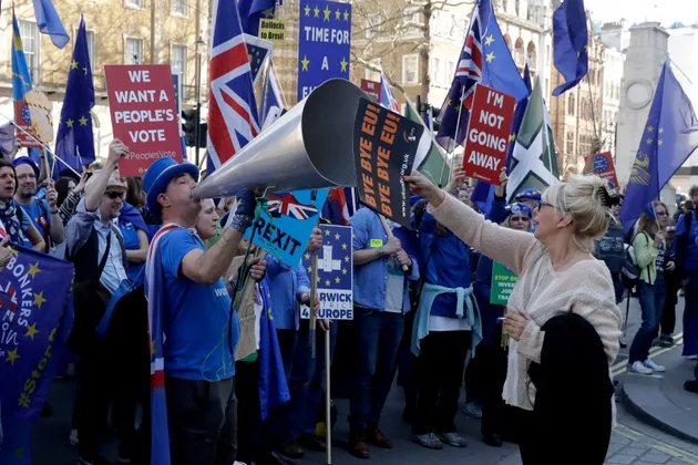 A supporter of Britain's departure from the European Union, at right, holds a placard up in front of supporters of remaining in the EU, including Stop Brexit Man, Steve Bray, with his foghorn, outside Parliament in London, Wednesday, Feb. 27, 2019.