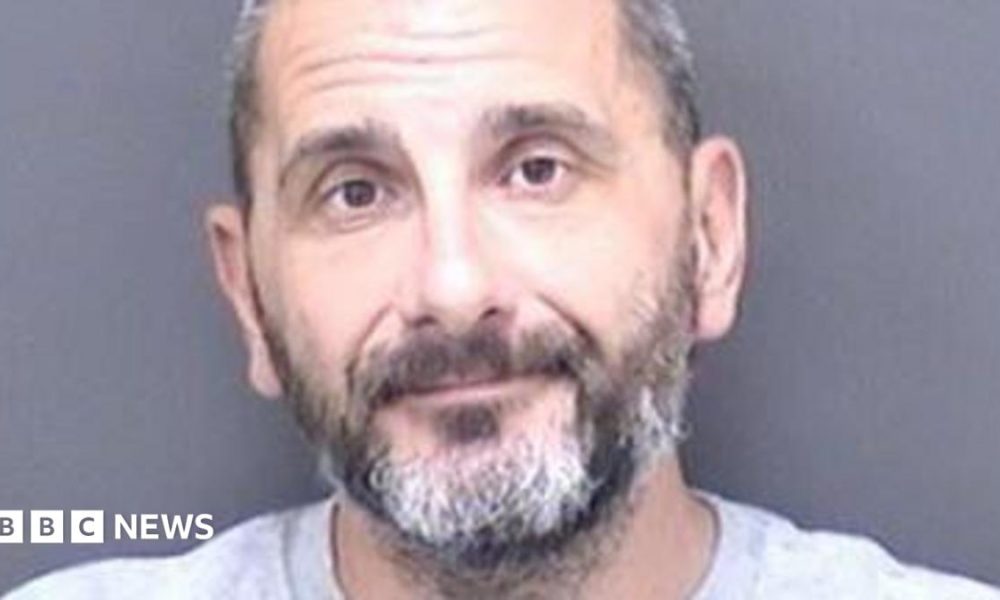 A custody shot of Matthew Ashley Foster-Smith. He has short hair and a beard and is wearing a grey jumper.