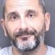 A custody shot of Matthew Ashley Foster-Smith. He has short hair and a beard and is wearing a grey jumper.