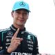 George Russell looks at the camera and points his index figure upwards