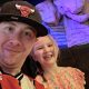 A man in a red and white football shirt and baseball cap smiles next to a younger girl in a pretty flowery dress