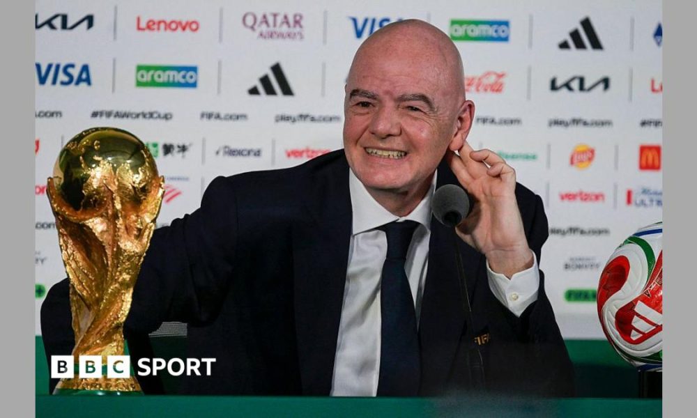 FIFA president Gianni Infantino, in dark suit and tie and white shirt, speaks next to the World Cup trophy and a football during a news conference on the eve of the opening match of the 2026 World Cup