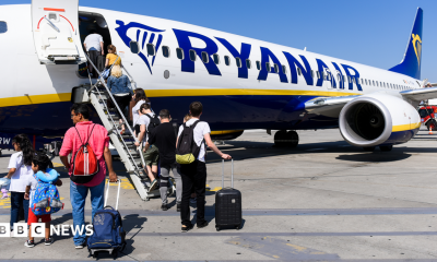 Passengers incluidng children boarding a Ryanair aircraft using the steps at the front of the plane on a sunny day with blue skies