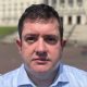 Dr David Farren, a man with dark hair, wearing a blue shirt, standing in front of Stormont Parlaiment Buildings.