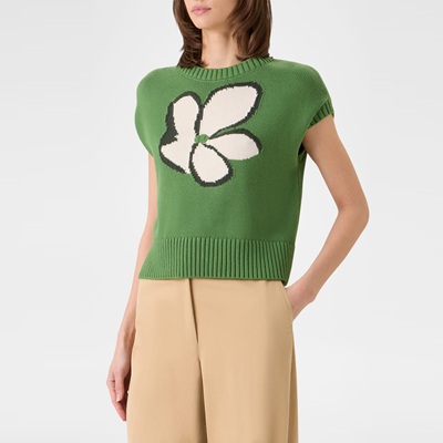 A woman wearing a bright green cap-sleeve sweater with a white flower on it, and khaki-colored pants