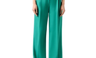 A woman (lower half of body shown) wearing green pants, a black top, and black flats