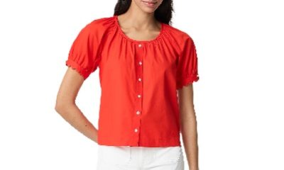 A woman wearing a bright orange button-front shirt and white shorts