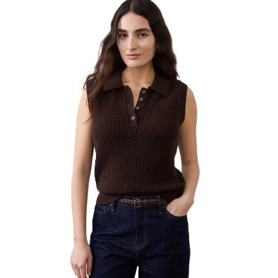 A woman wearing dark blue jeans, a brown belt, and brown crochet sleeveless top