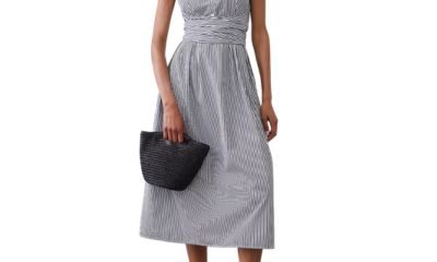 A woman wearing a sleeveless white-and-navy striped shirtdress and black flats. She is carrying a black woven bag.