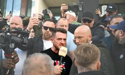 Tommy Robinson in a crowd speaking into a microphone, surrounded by people and cameras, before the riot kicked off