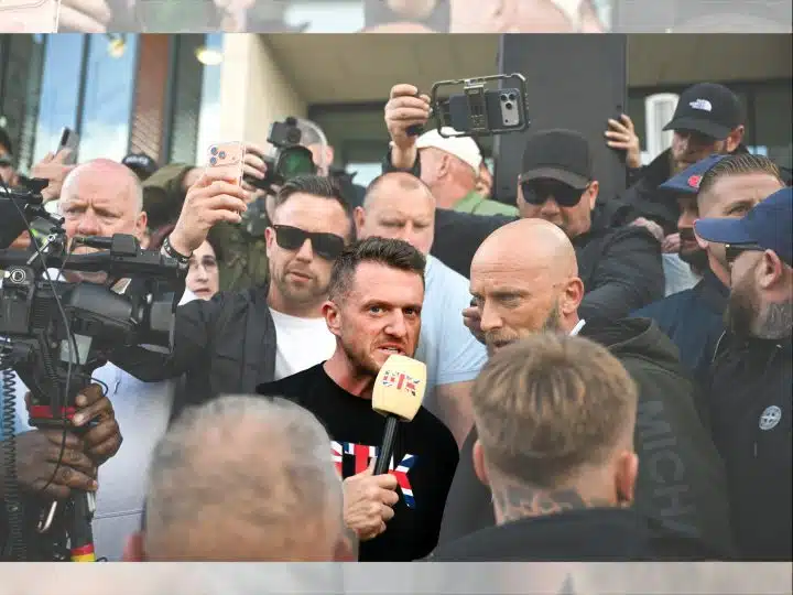 Tommy Robinson in a crowd speaking into a microphone, surrounded by people and cameras, before the riot kicked off