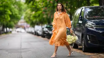 PARIS, FRANCE - MAY 10: Ketevan Giorgadze @katie.one wears gold earrings, a long buttoned coral loungewear linen The Sleeper dress with puffy sleeves, gold rings, a wicker with brown shiny leather detail Le Panier Soleil Jacquemus tote-bag, white strappy low heeled Raye sandals, on May 10, 2021 in Paris, France. (Photo by Edward Berthelot/Getty Images)
