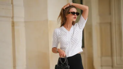 Segolene Hyppolite wears sunglasses, a white wool cardigan / top from Agnes B, a white flower shaped bracelet, a Chanel bag with floral texture / details, black pants from Agnes B, during a street style fashion photo session, on May 12, 2024 in Paris, France.