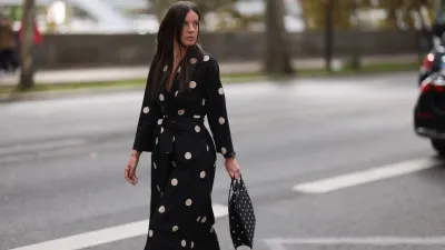 A Fashion Week guest is seen wearing round diamond stud earrings; a long-sleeved black midi dress with white polka dot pattern, notched lapels, and a tie belt; a gold bangle; a rose gold and black watch from Rolex; a gold ring; and a rectangular black handbag with a white polka dot pattern before the Elie Saab Womenswear Spring/Summer 2025 Show as part of Paris Fashion Week on September 28, 2024 in Paris, France.