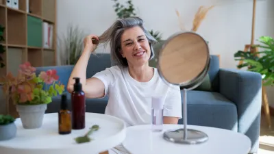 Smiling woman practicing beauty routine with mirror in home living room