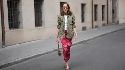 MUNICH, GERMANY - APRIL 28: Annette Weber is seen wearing an olive green cotton field jacket with a relaxed fit, button front closure and multiple flap patch pockets from AG Jeans; a white cotton crew neck top with a fitted silhouette from Brunello Cucinelli; a red satin longuette skirt with a straight silhouette and white polka dot print from Glamometer x Seidensticker; brown calfskin