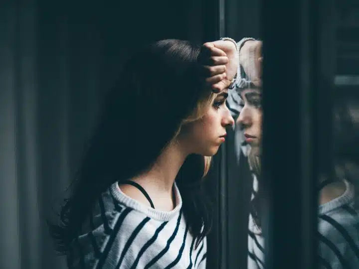 Stock image of girl looking through window, illustrating mental health outcomes
