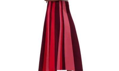 A woman wearing a white top, black sandals, and skirt with vertical stripes of reds and pinks