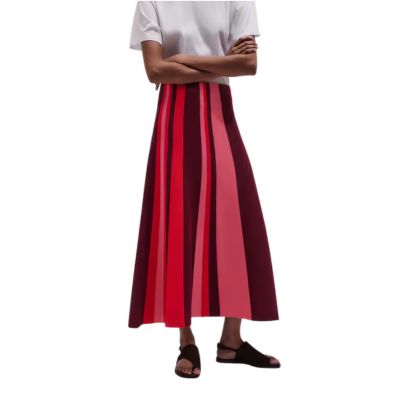 A woman wearing a white top, black sandals, and skirt with vertical stripes of reds and pinks