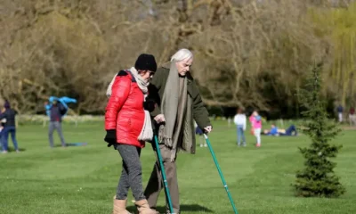 Carers Week: An older pair, one with two crutches, and the other locking their arm, walk and enjoy the spring sunshine at Mottisfont one of the National Trust parklands on 21 March 2020 in Romsey, UK