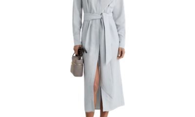 A woman wearing a midi length light blue dress and sandals, holding a light brown handbag