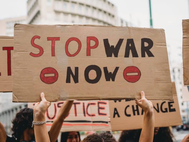 Hands holding a home made placard saying Stop War Now