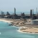A file photo of Aramco's Ras Tanura oil refinery and oil terminal, which lies along a stretch of coast. The site comprises a network of several tall chimney-shaped structures and smaller buildings. It is daytime and the water along the coastline is a clear blue.