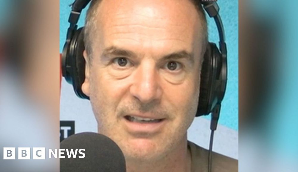 A man with short hair looks into the camera as he talks into a microphone