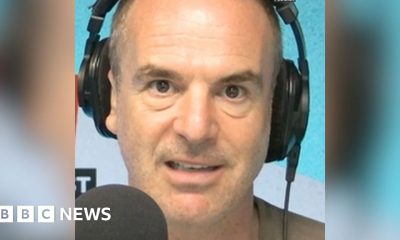 A man with short hair looks into the camera as he talks into a microphone