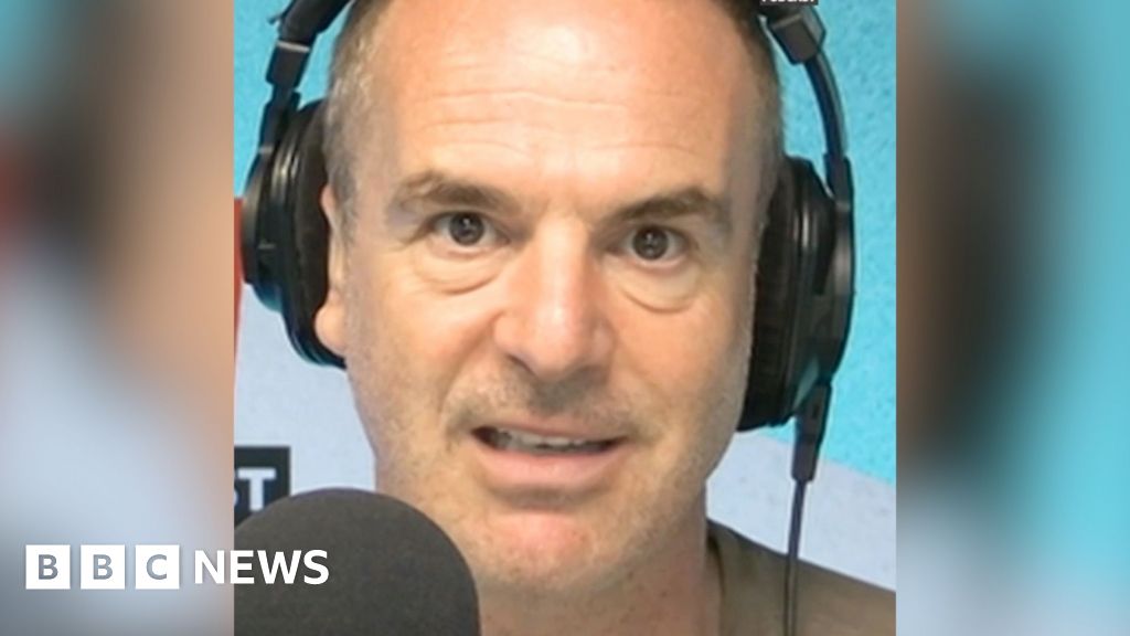 A man with short hair looks into the camera as he talks into a microphone